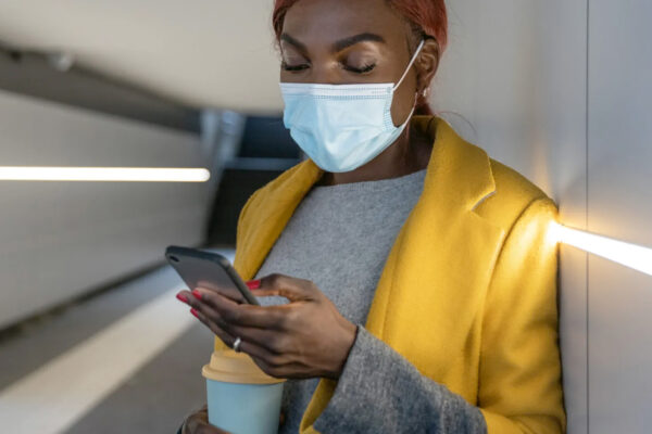 A woman wearing a surgical mask checking her phone.