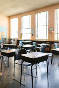 A bright, empty classroom with arranged desks and chairs, illuminated by natural sunlight.